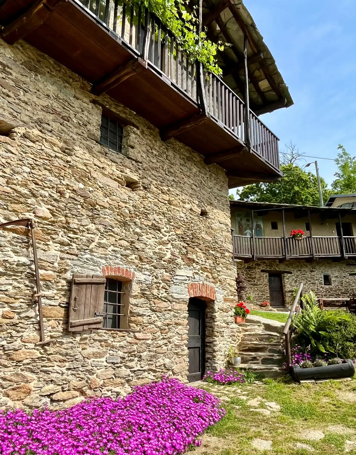 Facciata in pietra delle Baite del Bric, con balcone in legno e fiori